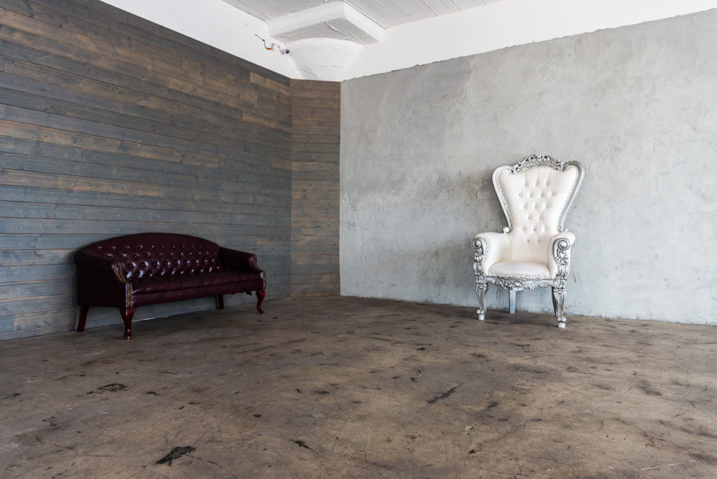 Photo and Video studio with concrete textured wall, red sofa and white extra large chair available for rental In Los Angeles