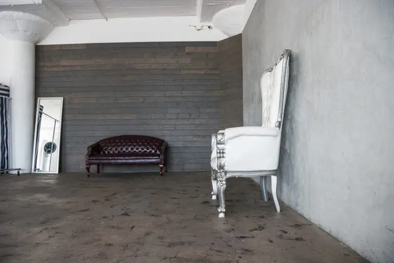 Photo and Video studio with concrete textured wall, red sofa and white extra large chair available for rental In Los Angeles
