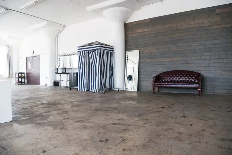Photo and Video studio with concrete textured wall, red sofa and white extra large chair available for rental In Los Angeles